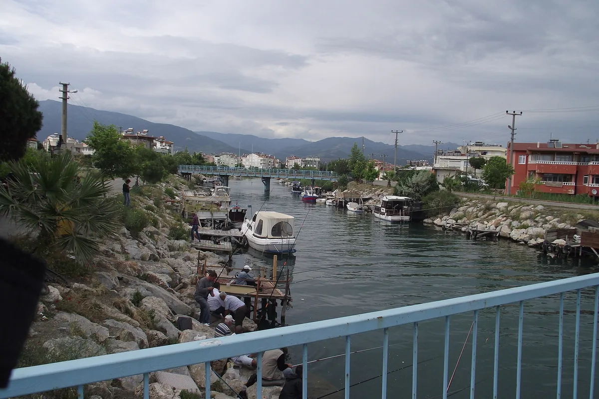 Akçay'ın küçük tekne kanalı, iskeledeki balıkçılar ve arka planda Kaz Dağları silüeti
