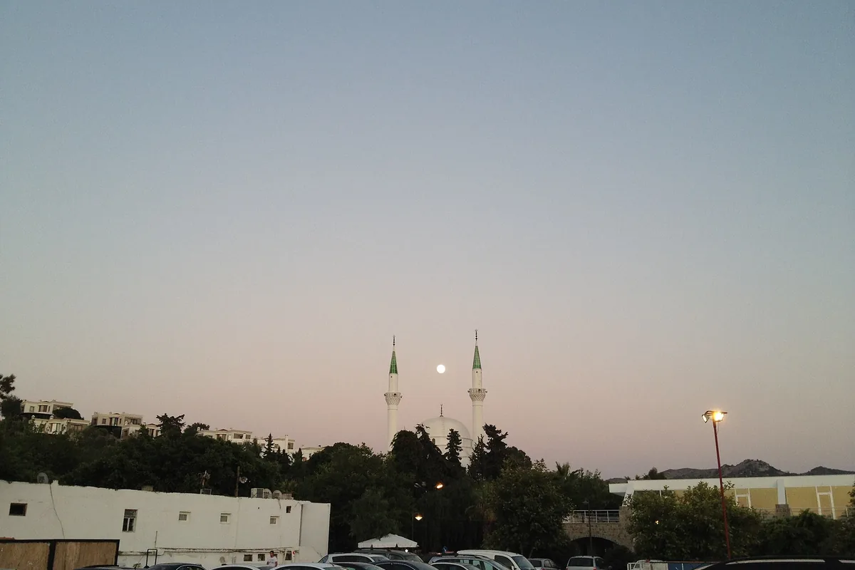 Alacakaranlıkta iki minareli bir caminin siluetiyle beldenin akşam görünümü