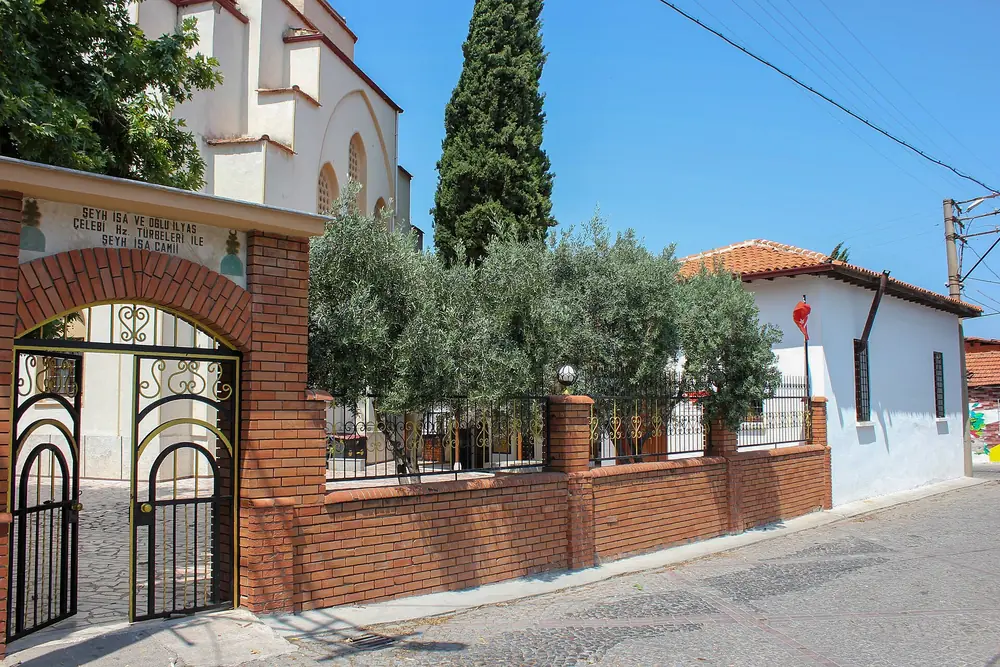 Akhisar'ın Şeyhisa Mahallesi'ndeki Şeyh İsa Camii'nin bahçe kapısı, zeytin ağaçları ve türbe tabelası