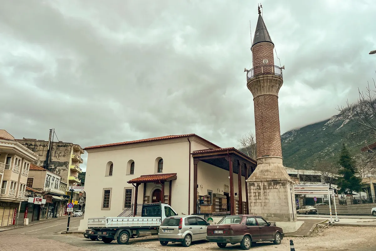 Kırkağaç'taki Karaosmanoğlu Camii'nin taş minaresi, kırma çatısı ve önündeki meydan